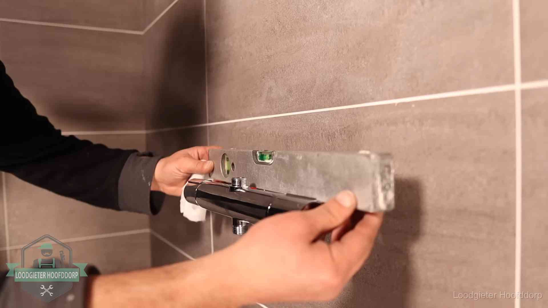 Loodgieter lijnt een douchekraan uit met een waterpas in een woning in Hoofddorp