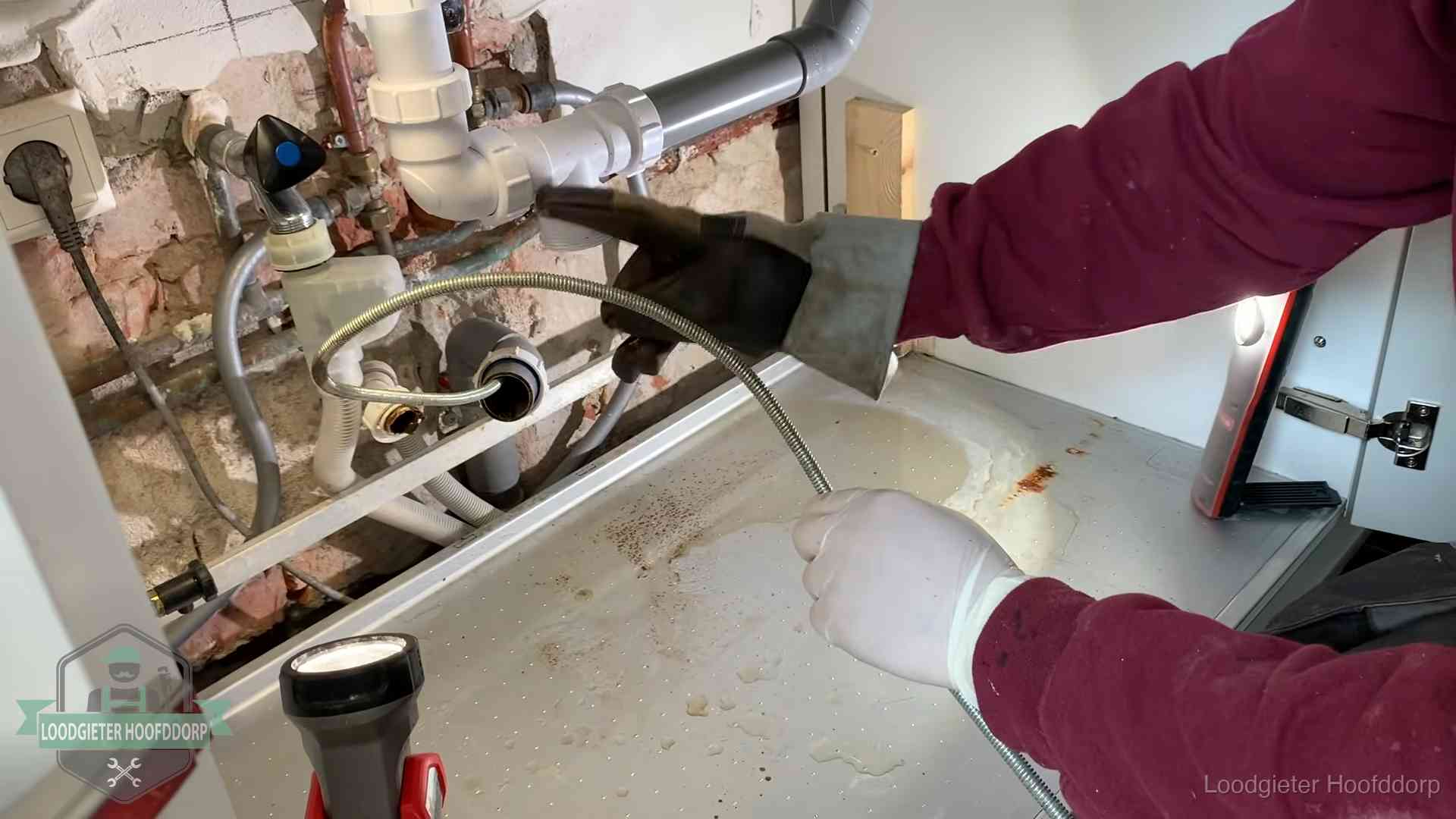 Ontstoppingsveer gaat in een geopende sifonaansluiting onder het aanrecht in Hoofddorp