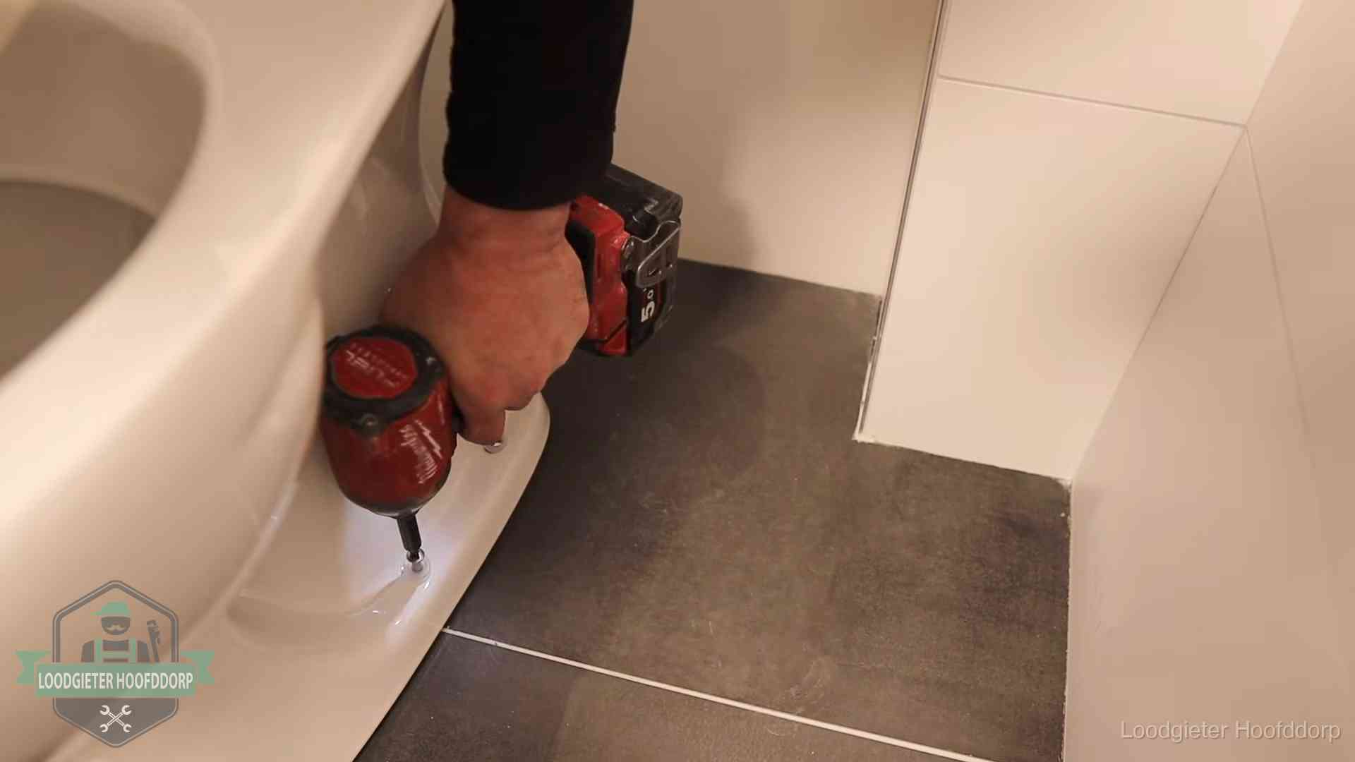 Kosten wc ontstoppen in Hoofddorp Loodgieter zet de voet van een wc-pot vast op de tegelvloer in Hoofddorp